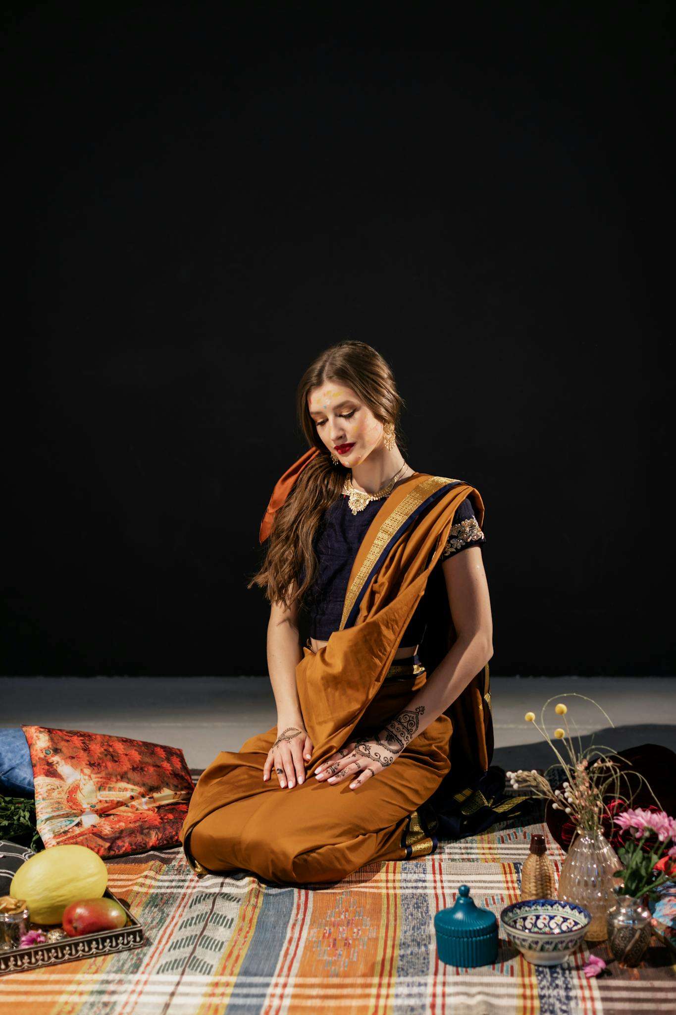 A woman in a sari sits gracefully with cultural artifacts, showcasing traditional grace.